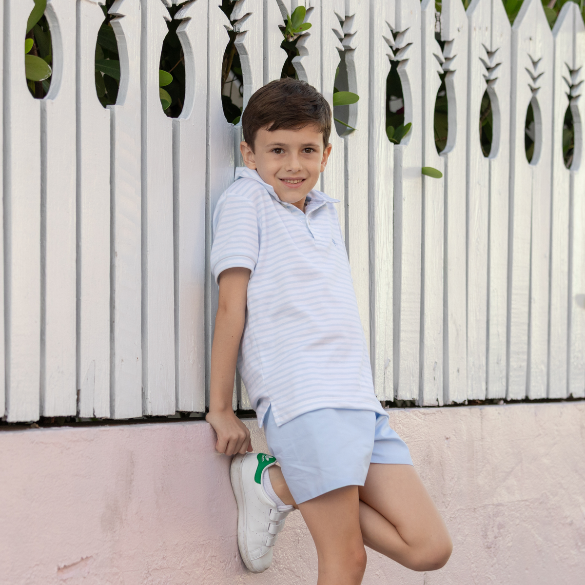 Three-quarter view of Robert shorts in Bailey’s Bay Blue on boy model, flat front and elastic back, leaning on white fence
