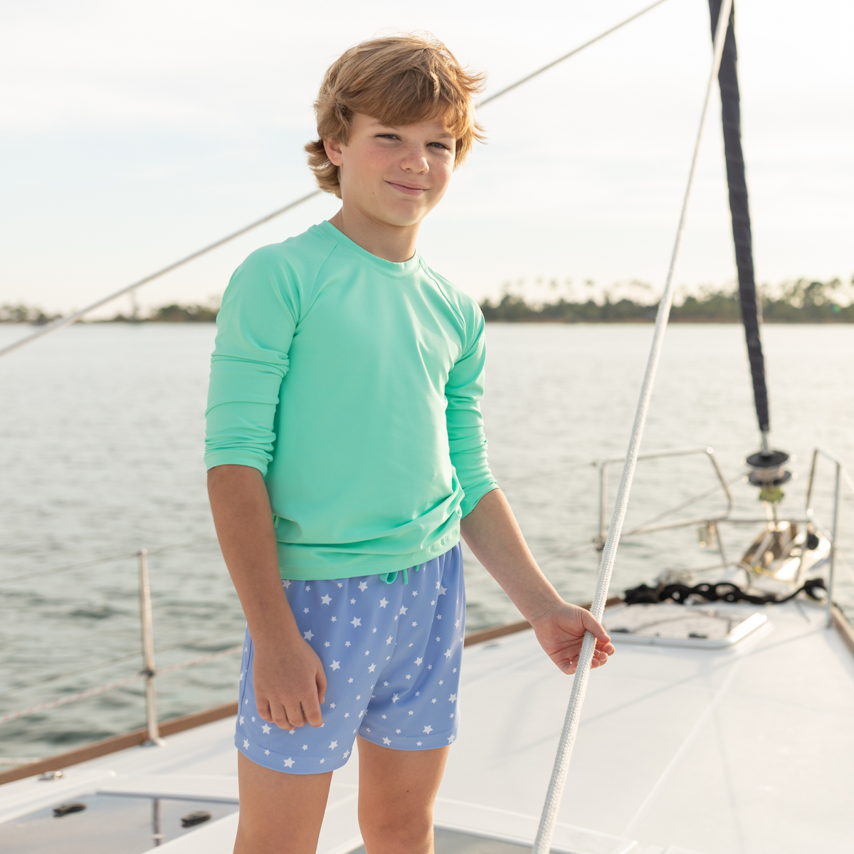 Front view of Tatum Trunks in blue star print showing above-the-knee fit and elastic drawstring waistband on a sailboat