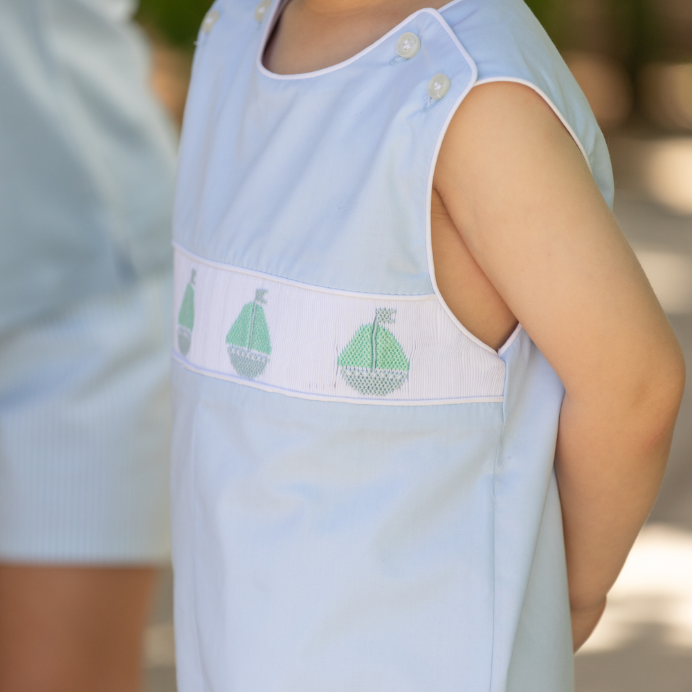 Side view of George Jon Jon in Bailey’s Bay Blue with hand-smocked sailboat band and shoulder buttons, blurred background