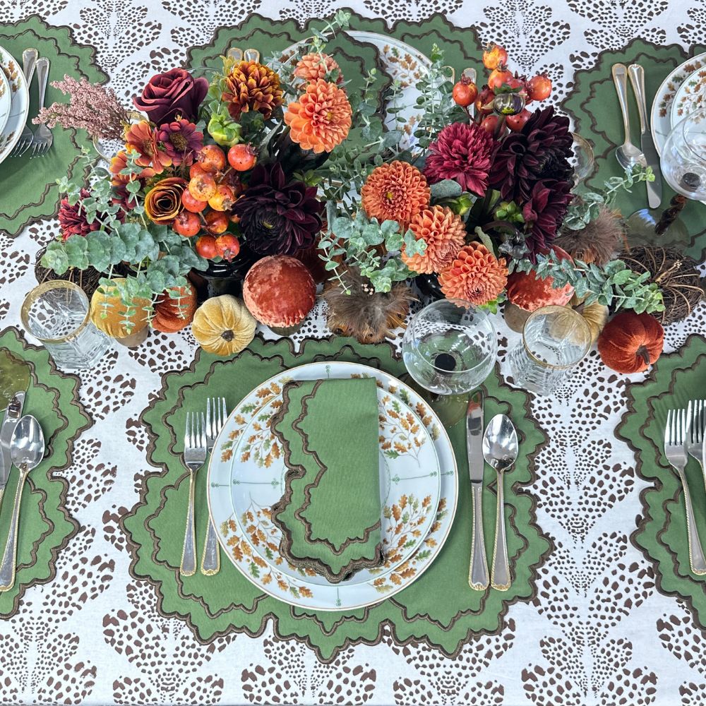 Decorative table setting with autumn-themed centerpieces, plates, and cutlery on a patterned tablecloth.Thanksgiving table, embroidered placemats.