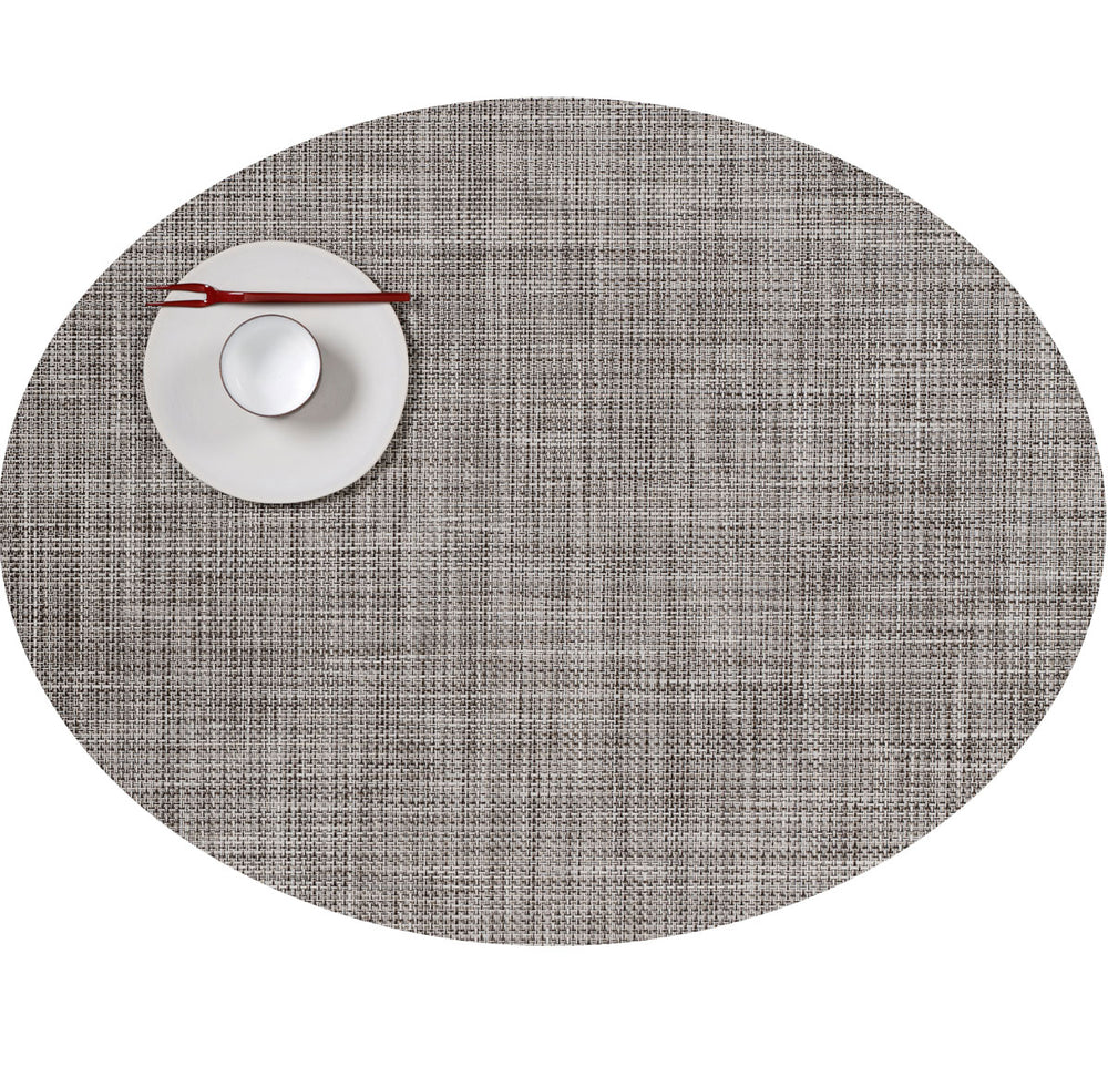 Top-down view of Mini Basketweave round placemat in Gravel showing woven texture with white saucer, cup, and red chopsticks