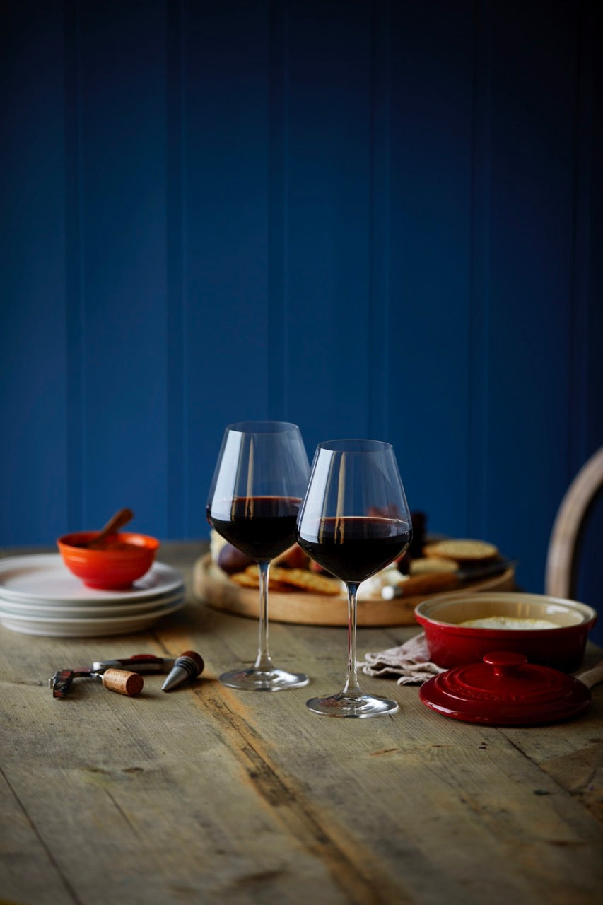 Red mini round cocotte with lid displayed on a dining table beside wine glasses and appetizers
