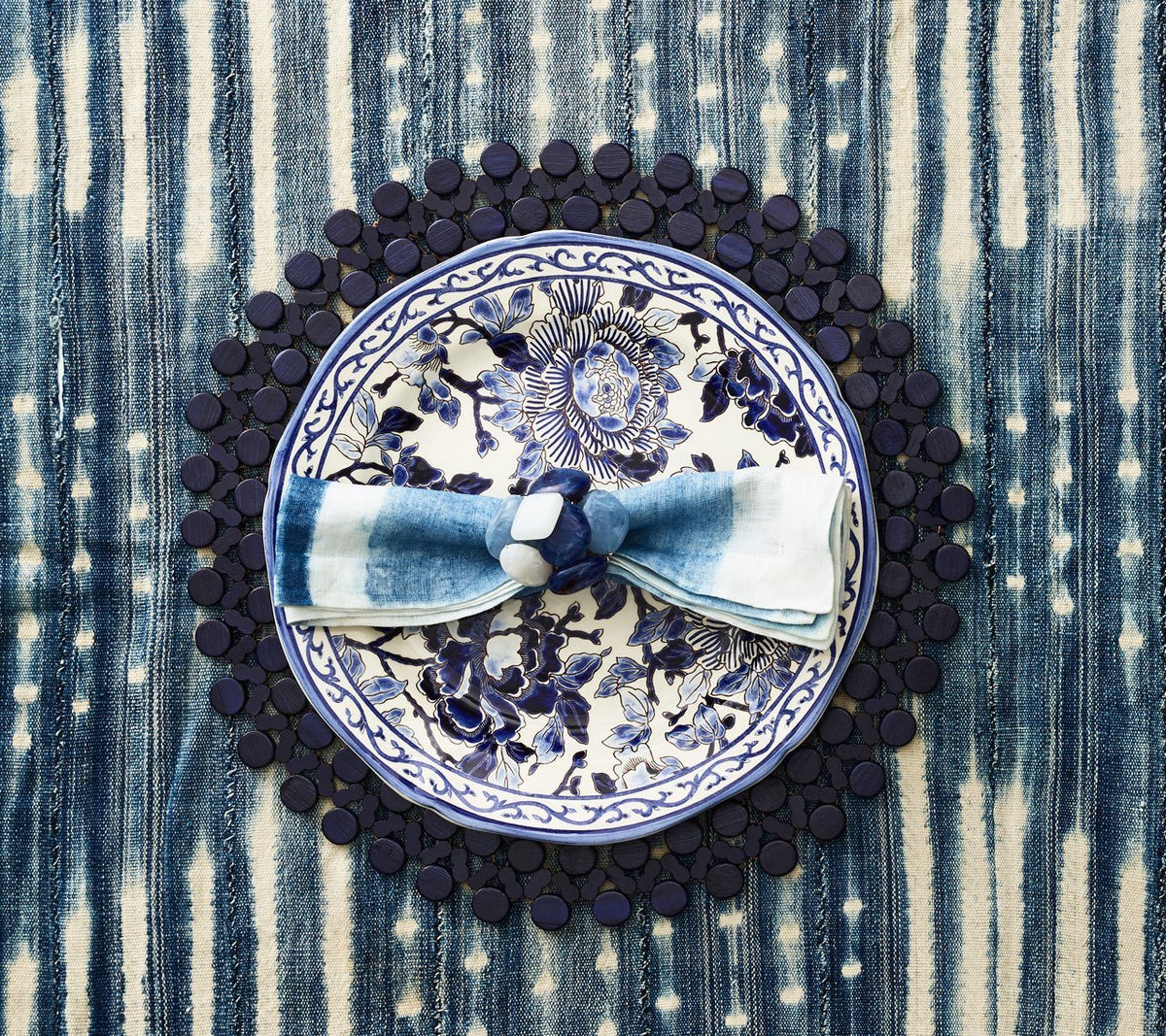 Top view of Round Bamboo Placemat in Navy Blue Set of 4 showcasing hand-strung bamboo beads beneath a floral plate