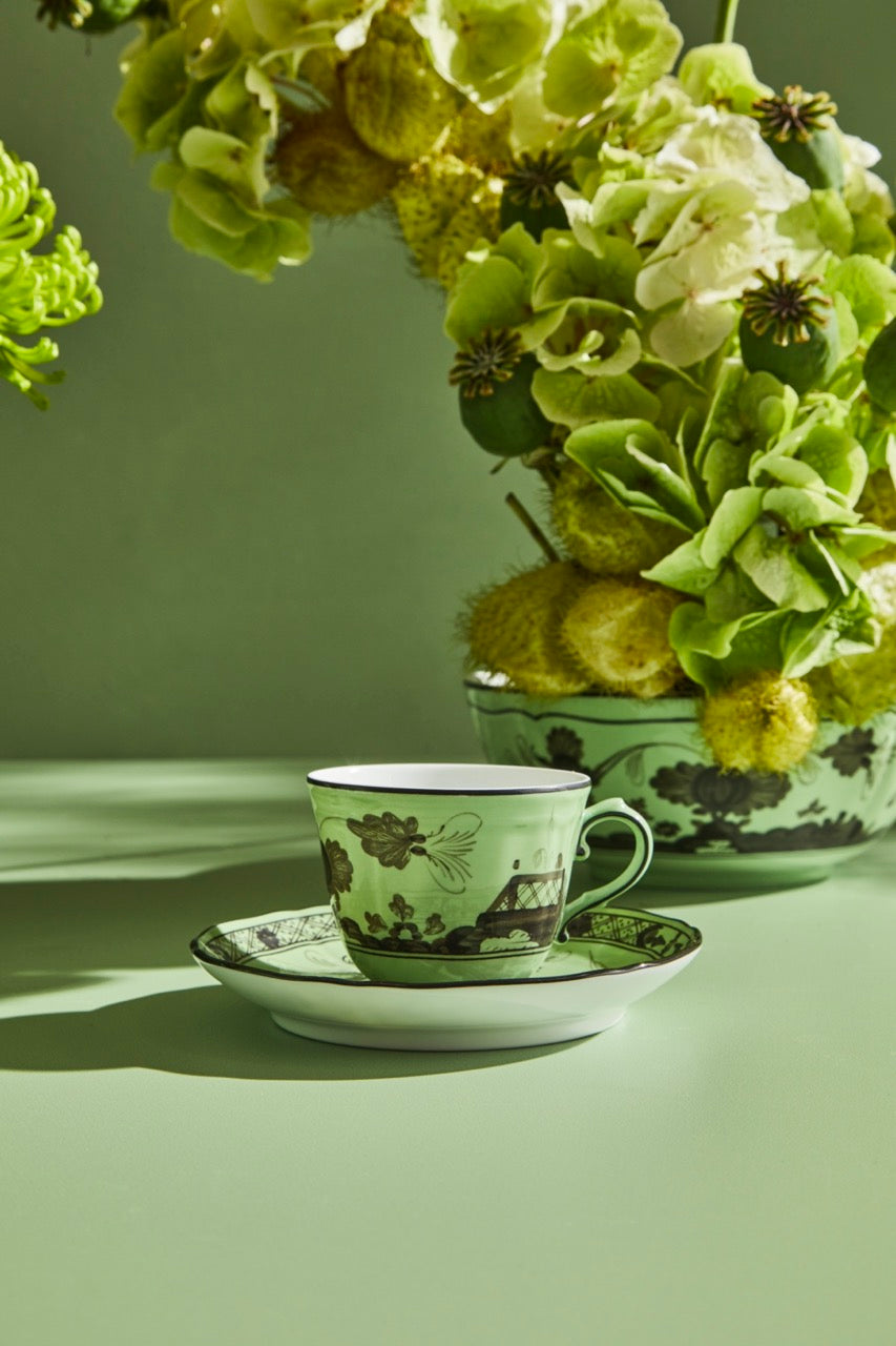 Front view of Oriente Italiano coffee cup and saucer in Bario green porcelain with dark floral motifs on a pale green table