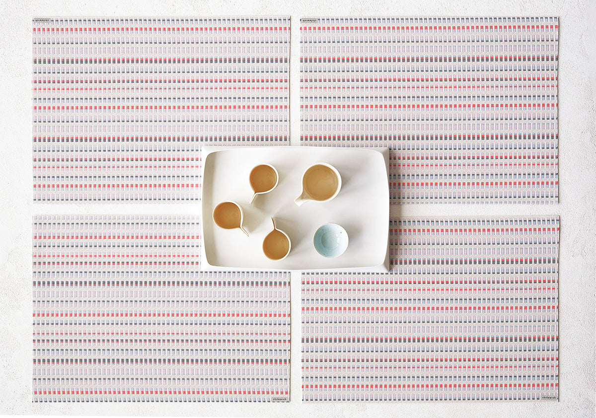 Overhead view of Tambour Placemats showcasing multicolored woven stripes around a serving tray on a white surface