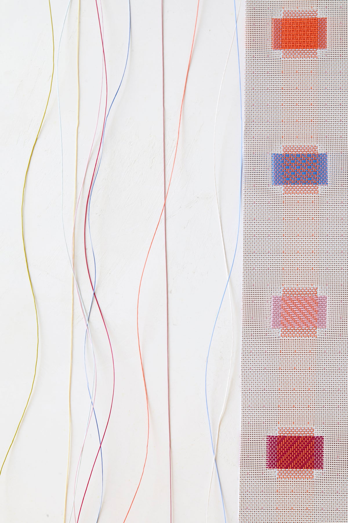 Close-up of Sampler Table Runner showcasing multicolored woven square motifs and trailing colorful yarns on a white background