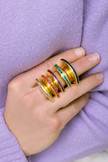 Close-up of hand wearing stacked Eclipse Rings with sculptural 18k yellow gold bands and colored gemstone inlays on a lavender sweater