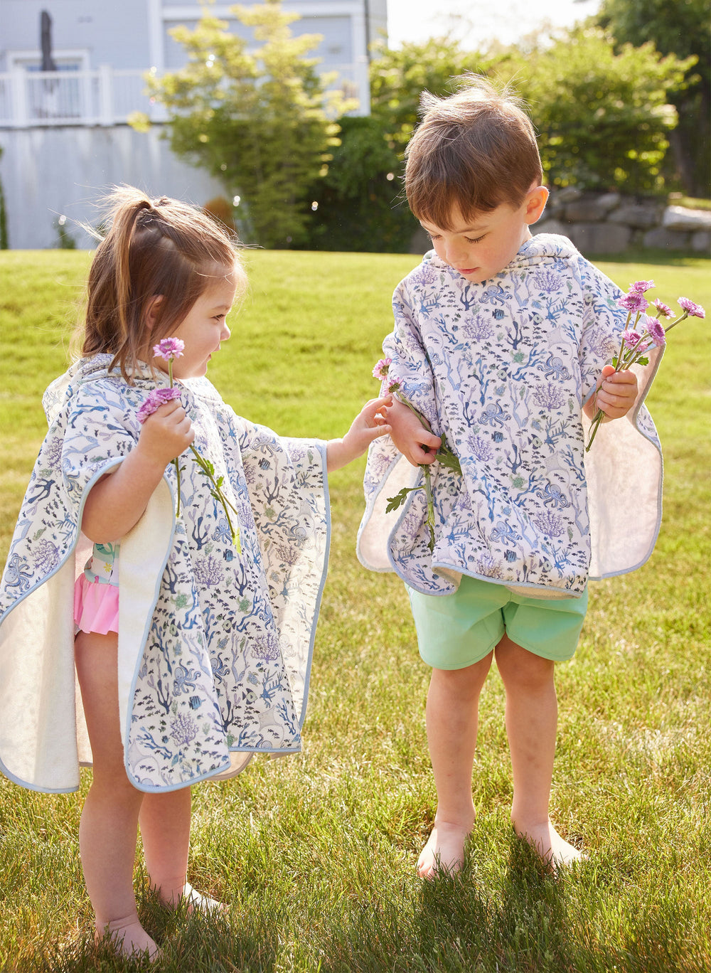 Three-quarter view of Coral Reef swim poncho on two toddlers showcasing hooded organic cotton terry and blue coral print in sunny yard