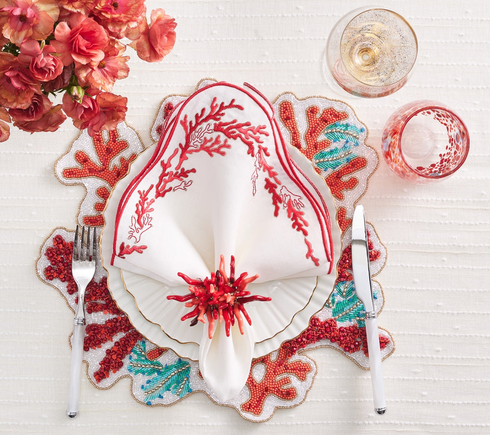 Top-down view of Amalfi napkin ring in coral showcasing red coral-shaped beads with a folded white napkin on beaded placemat