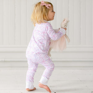 Side view of a child wearing a pink ballet zip onesie, holding a bunny toy against a white paneled background