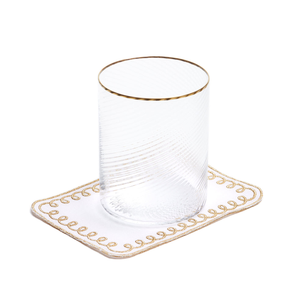Top view of Golden Loopy cocktail napkin on white Belgian linen with hand stitched gold loopy border and clear glass