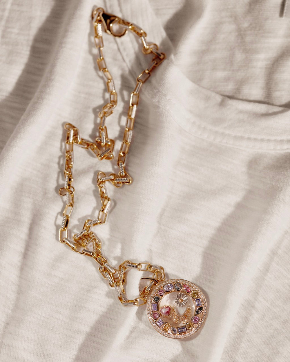 Close-up of Courage Daisy charm showing round gold pendant with multicolored stones on white fabric