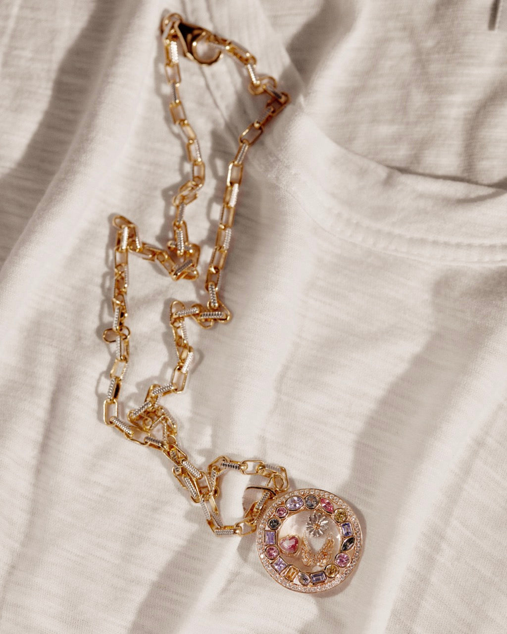 Close-up of Courage Daisy charm showing round gold pendant with multicolored stones on white fabric