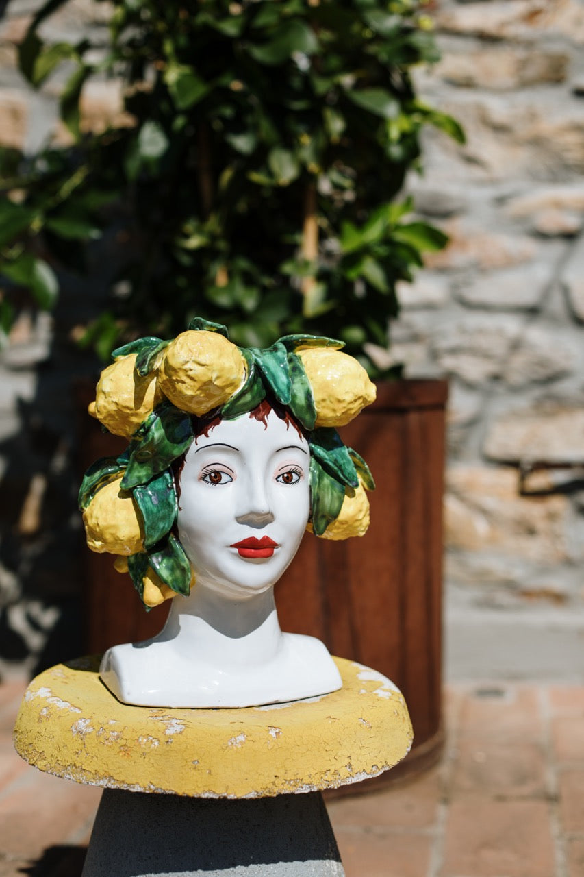 Front view of Sicilian Heads lemon head bust with hand painted lemons and green leaves on a white face with red lips