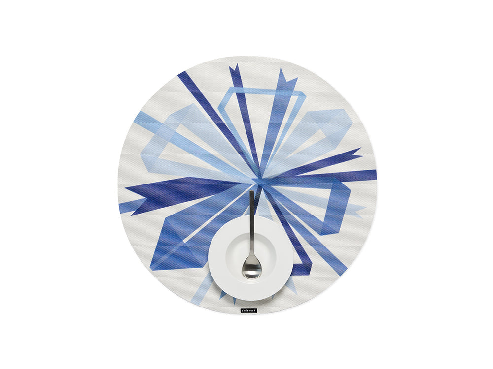 Top view of Bow placemat in Frost showing blue geometric bow print on white woven background with plate and spoon at center