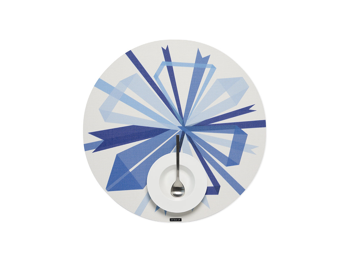 Top view of Bow placemat in Frost showing blue geometric bow print on white woven background with plate and spoon at center