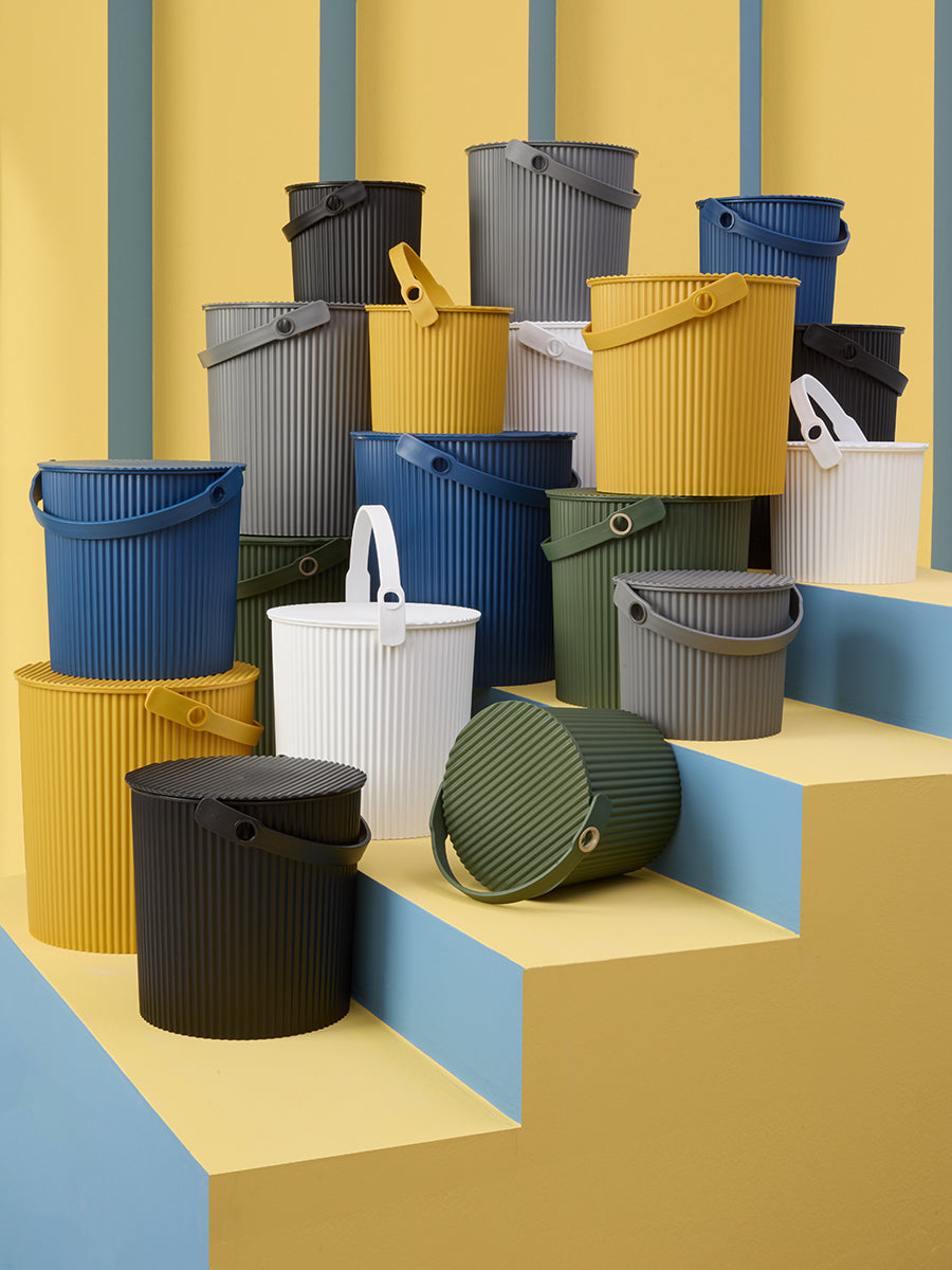 Stacked Hachiman Bucket Large showing ribbed body, top handle, and lids in multiple colors on a yellow stepped backdrop