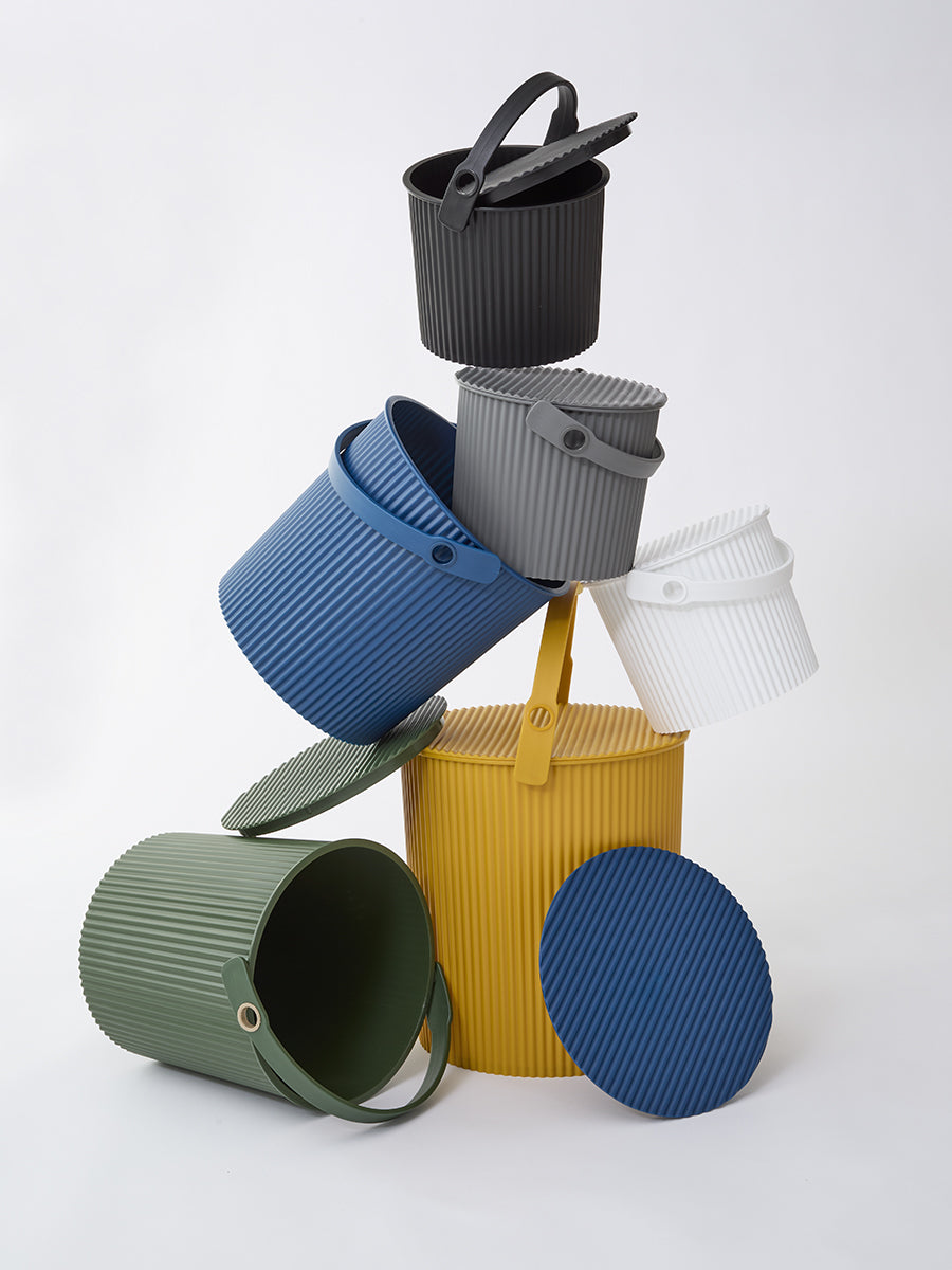 Studio view of Hachiman Bucket Extra Large mustard with other colors, showing ribbed exterior, lid, and handle
