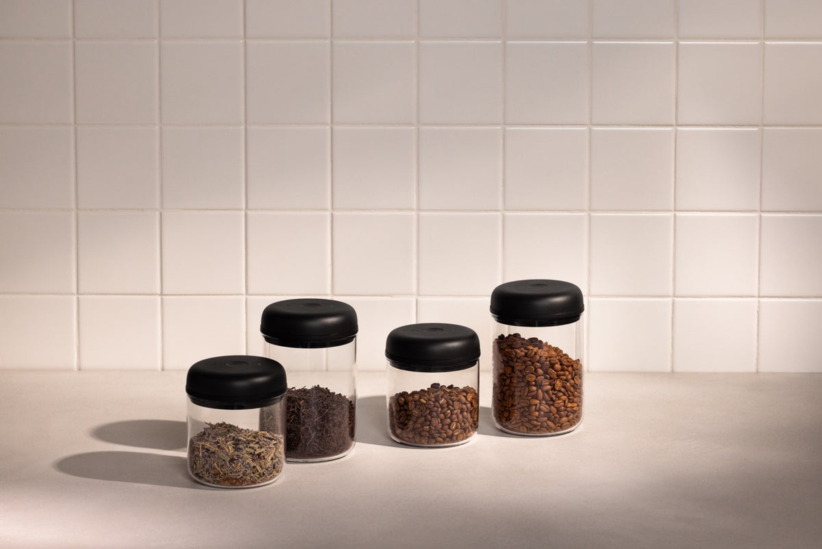 Front view of Electric Atmos Vacuum Canisters showcasing clear glass canisters with black lids in two sizes holding coffee beans and tea on a tiled countertop
