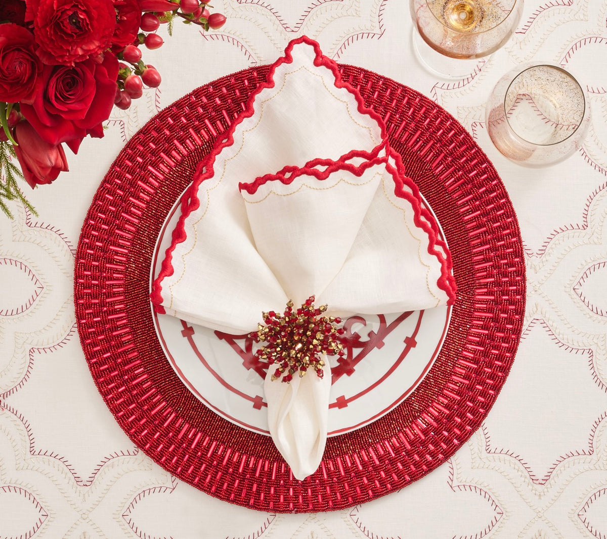 White linen napkin arranged on a festive red and gold place setting with flowers and glassware