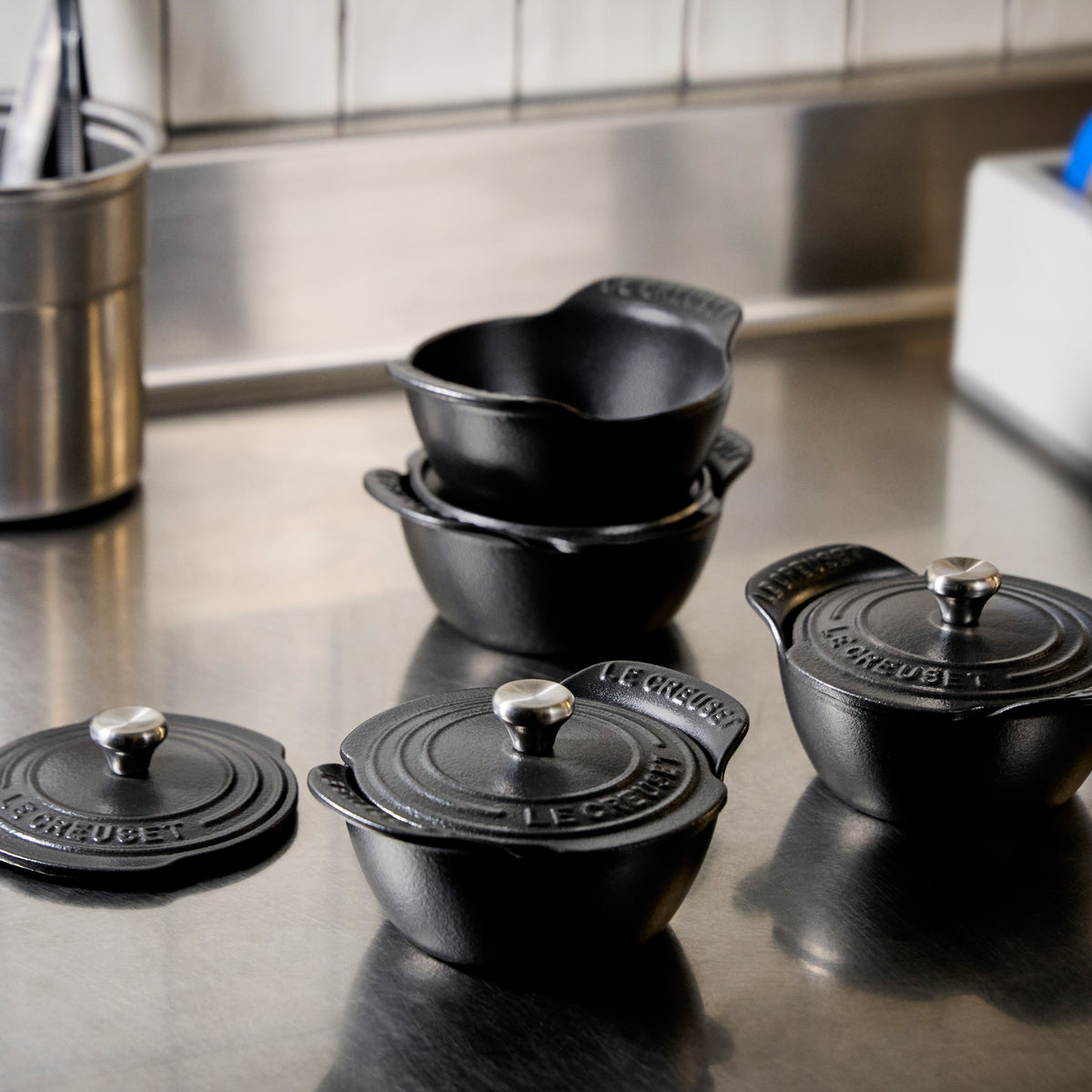 Close-up view of Mini Round Cocotte set of 4 showcasing matte black enamel and sterling silver knobs on a kitchen counter