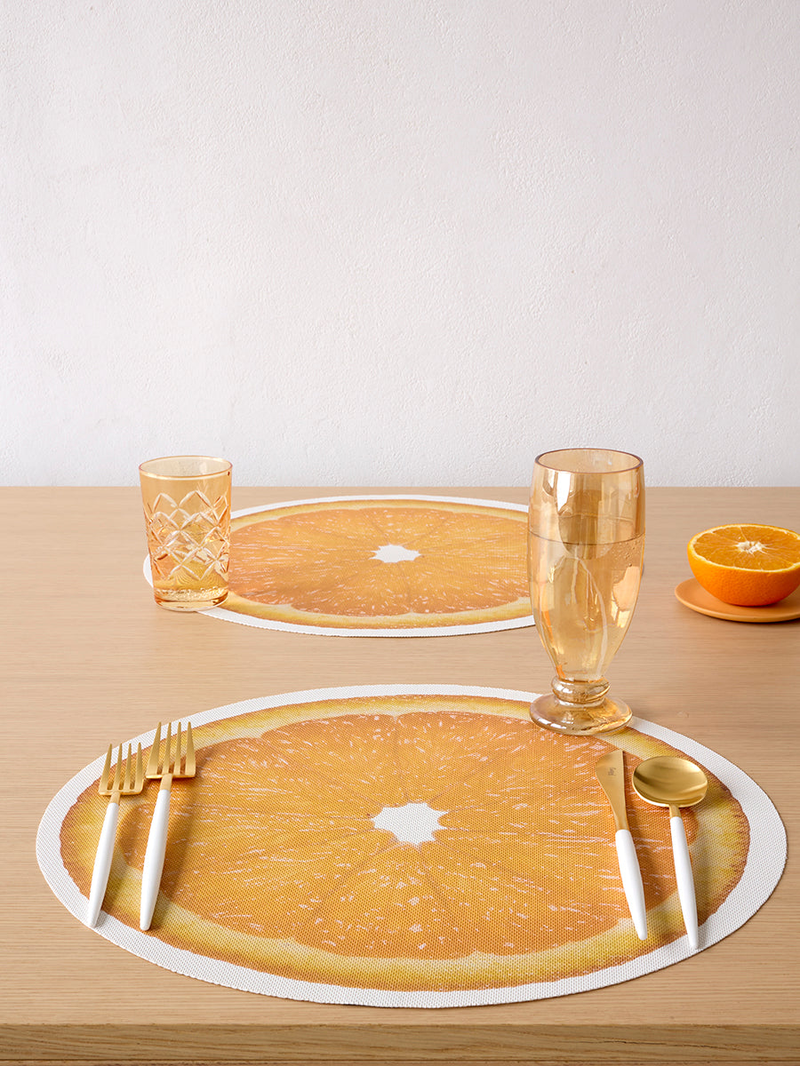 Front view of Citrus Placemat in Orange showing round citrus-slice print and textured weave on a light wood table