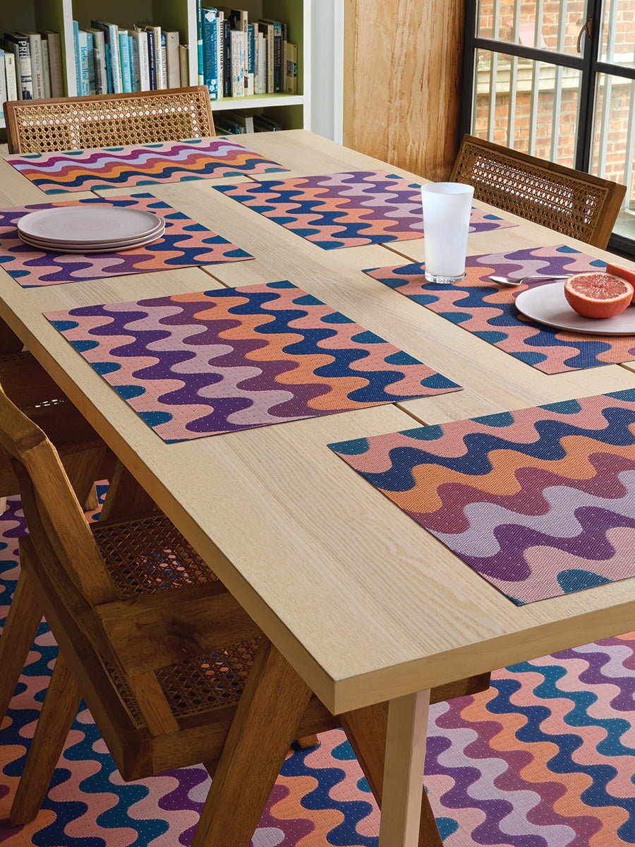 Angled overhead view of Wiggle rectangular placemat in Heatwave showcasing wavy multicolor pattern on a wood table