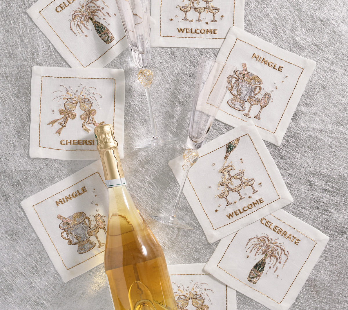 Overhead view of Cheers Cocktail Napkins, set of 8, showcasing white linen with gold and silver celebration embroidery