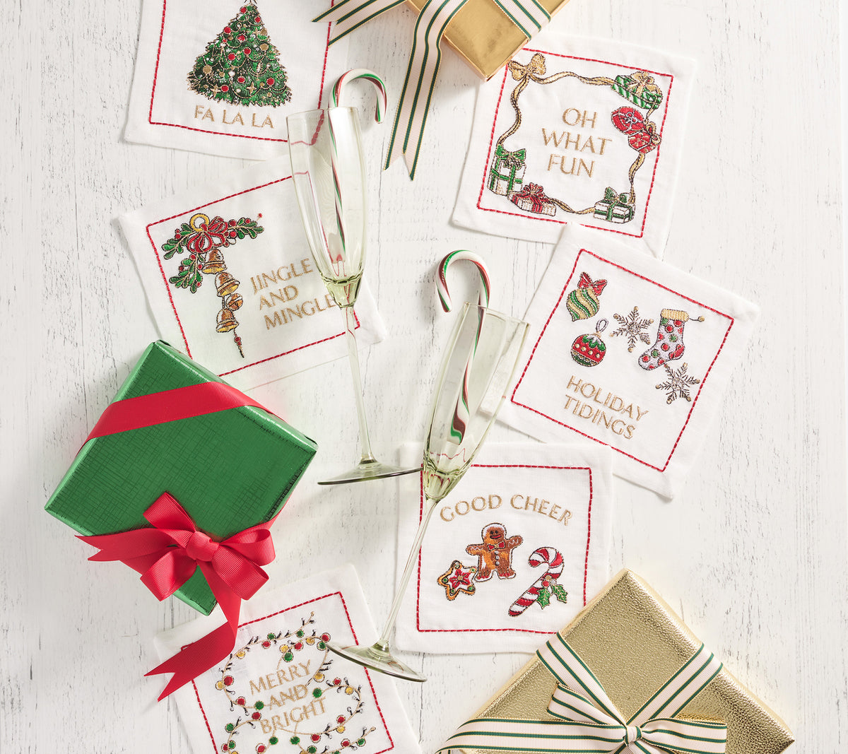Overhead view of six white linen Merry and Bright cocktail napkins showcasing embroidered holiday greetings on tabletop