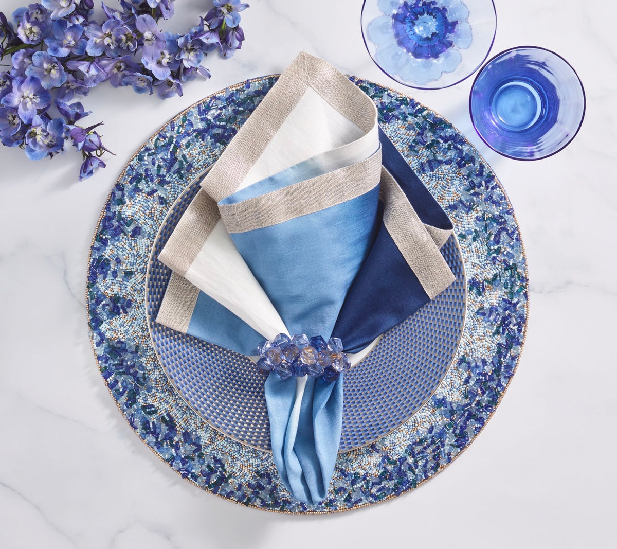 Top view of Lagoon Placemat in Navy and Blue showcasing cobalt blue and silver beaded organic border on a marble tabletop