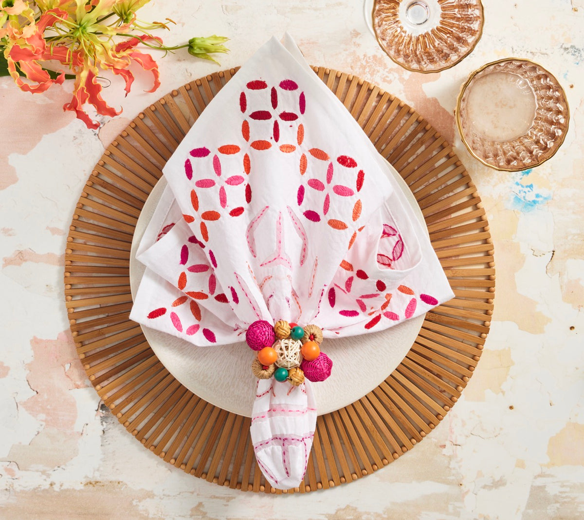 Brown Spoke bamboo placemat displayed beneath a plate with a folded embroidered napkin and colorful napkin ring on a styled table