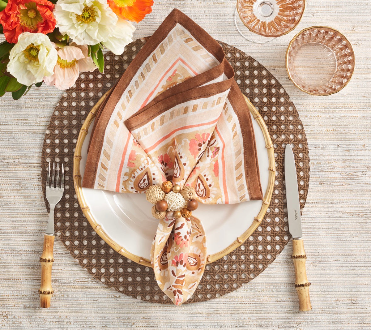 Brown Reed placemat anchors a styled table setting with a floral napkin, bamboo flatware, flowers, and glassware
