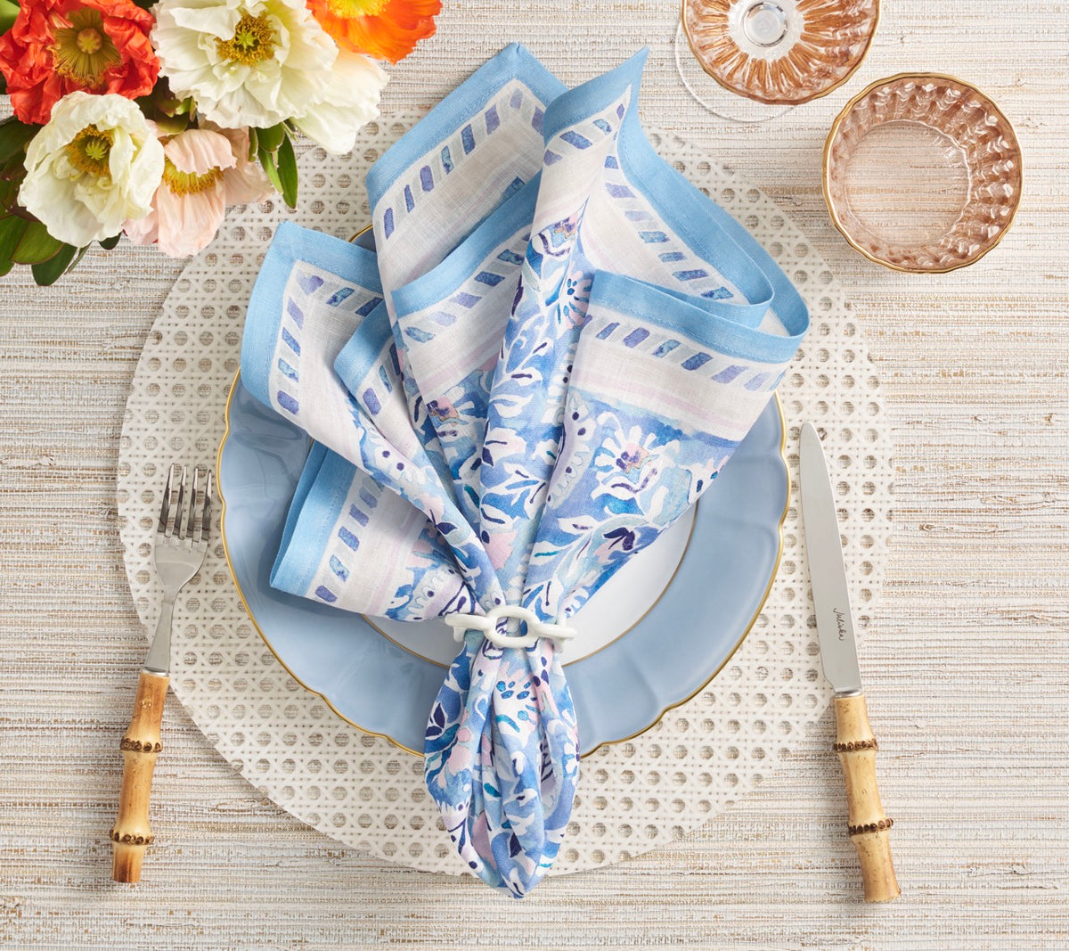 White Reed placemat displayed beneath a blue plate with floral napkin, wood-tone flatware, and glass bowls