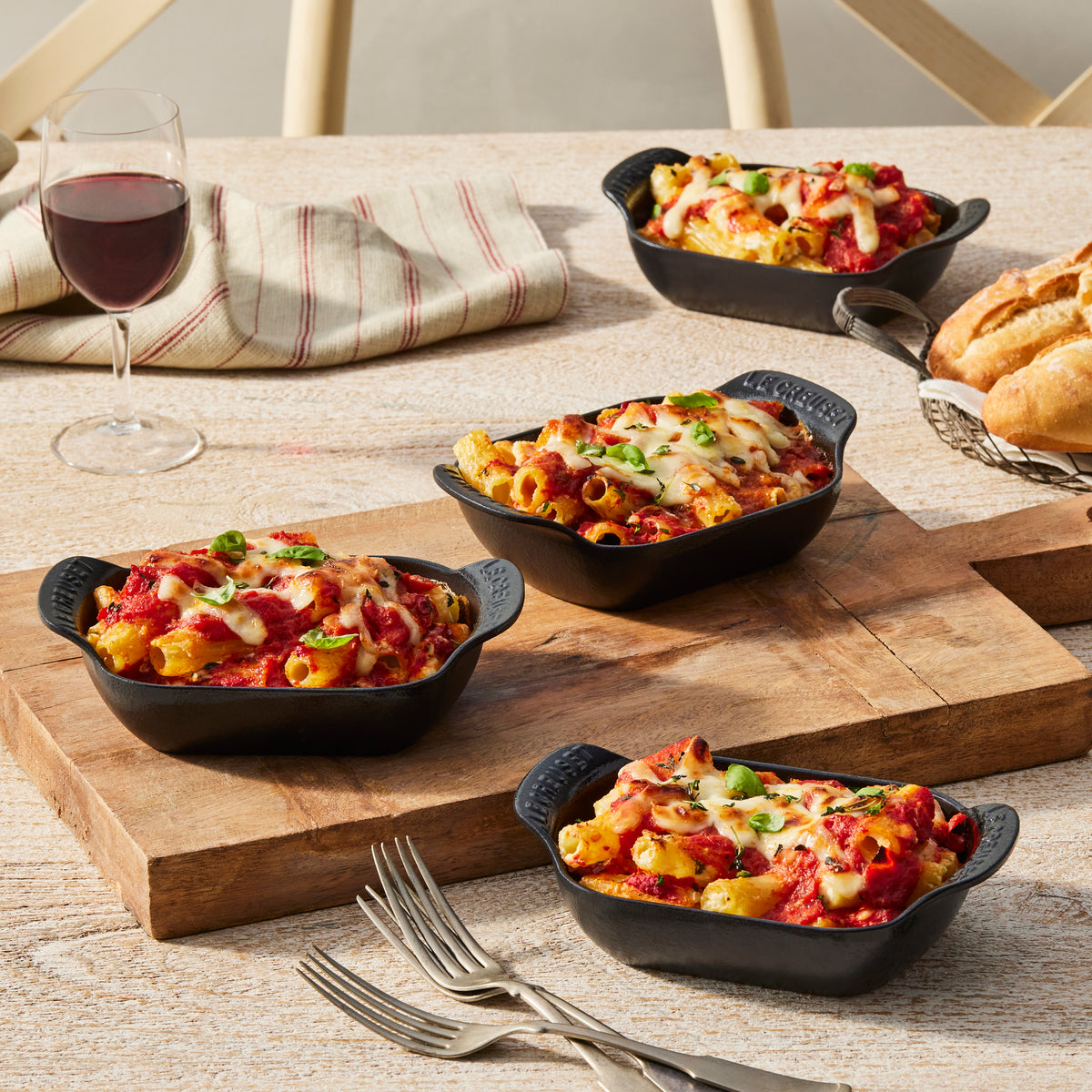 Mini rectangular bakers holding baked dishes on a rustic dining table with wine and tableware