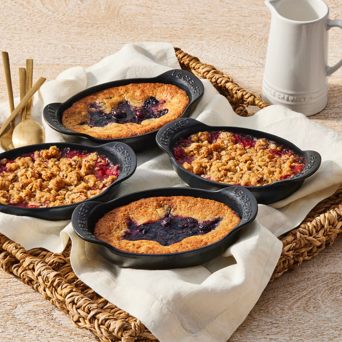 Front view of four Mini Oval Baker 1/3 qt dishes showcasing matte black enamel and baked desserts on a woven tray