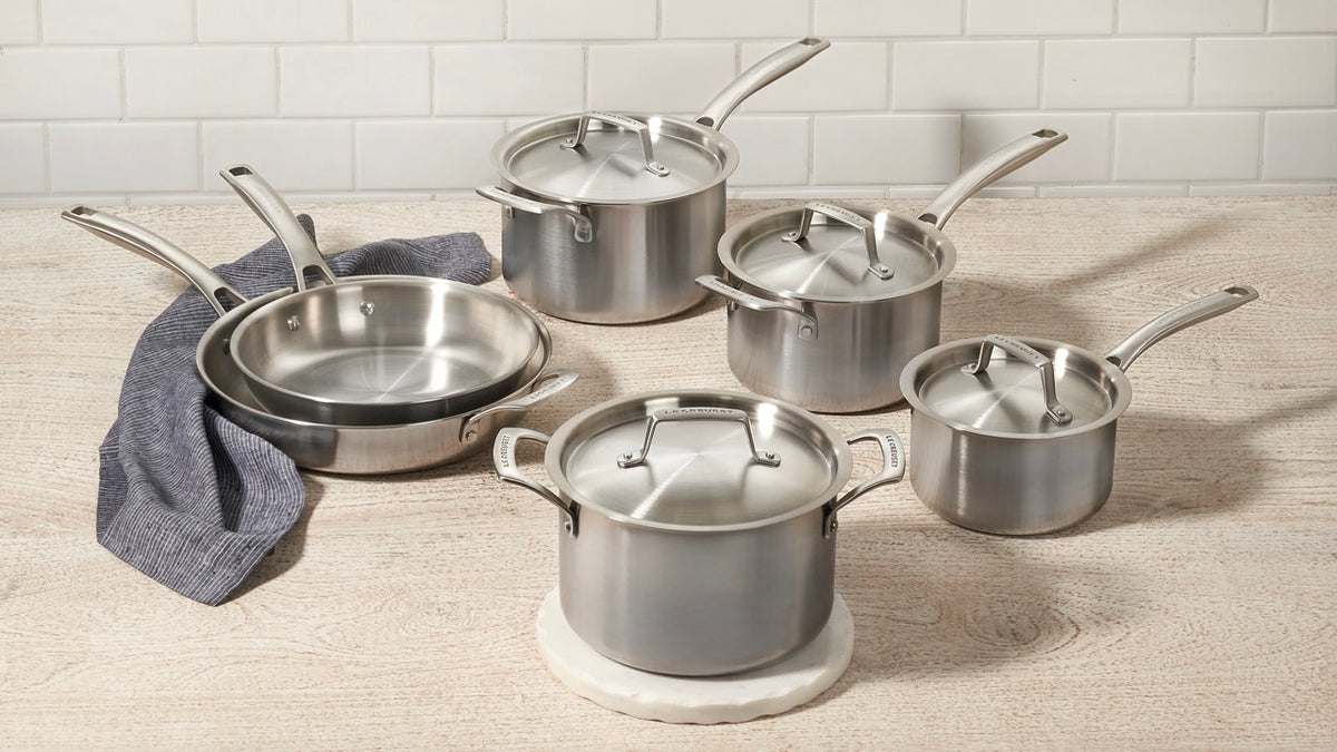 Angled top view of Essential stainless steel cookware with 10-inch frying pan and lidded pots showing brushed finish on wood
