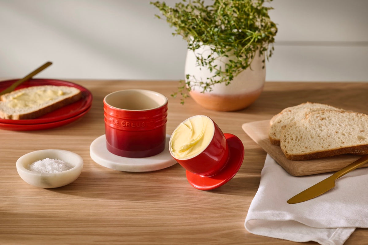 Angled view of Butter Crock 6 oz cerise with glossy stoneware and matching lid holding butter on wooden table