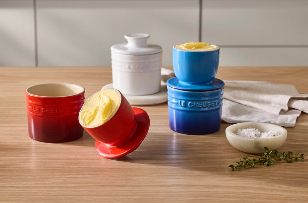 Front view of Butter Crock 6 oz showing inner cup of butter and airtight lid with red, blue, and white crocks on wood table
