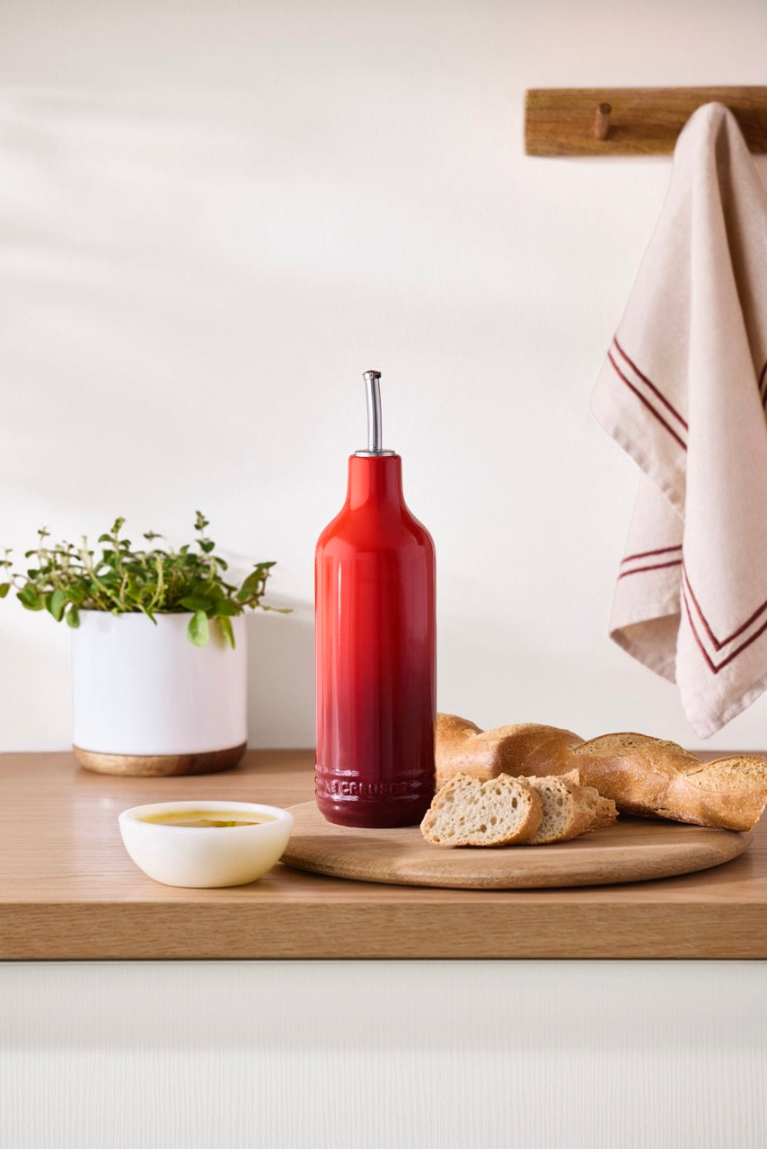 Front view of Signature Oil Cruet in Cerise showcasing stainless steel curved pour spout with kitchen countertop background