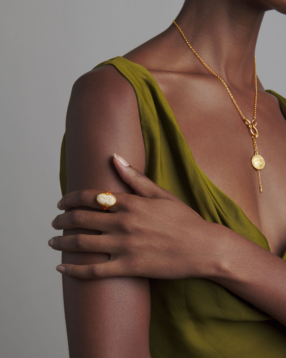 Close-up of The Cinched Cameo Ring on a model’s hand showcasing carved bone cameo and three carnelian stones with olive-green dress background