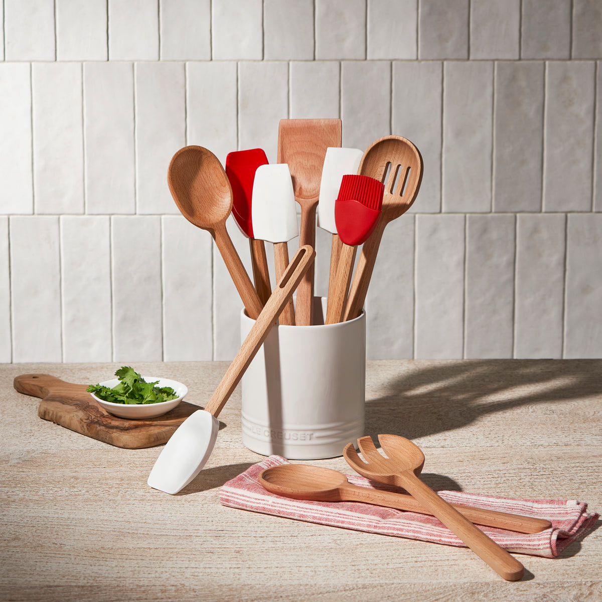 Front view of Signature Wood Serving Spoon and matching utensils showcasing curved beech bowl and smooth finish in a white crock on tiled countertop