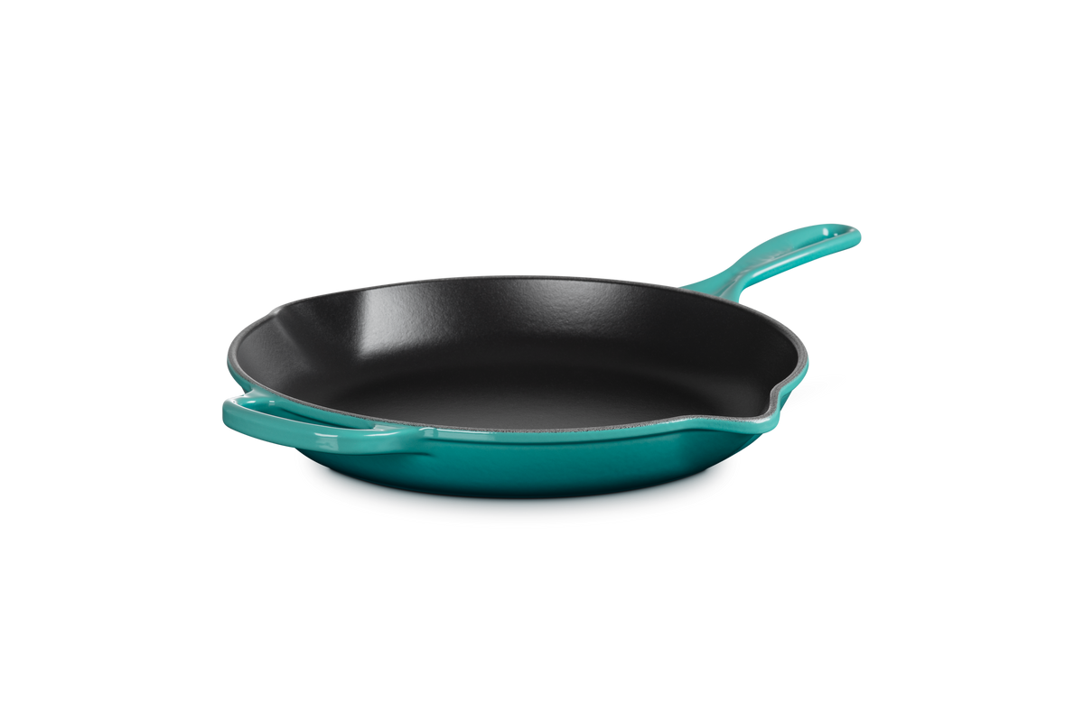 Angled view of Signature Round Skillet 10.25 in Riviera showing black satin enamel interior, dual pour spouts, and long handle on dark background
