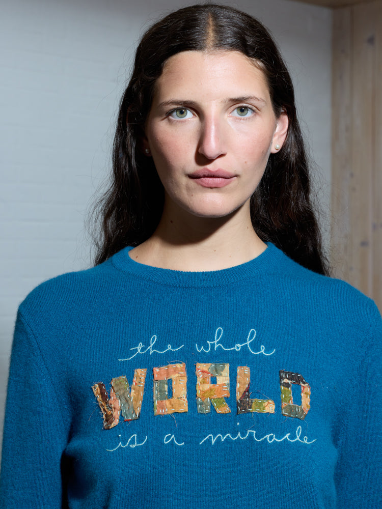 Front view of crewneck on model showcasing embroidered phrase the whole WORLD is a miracle with patchwork WORLD letters