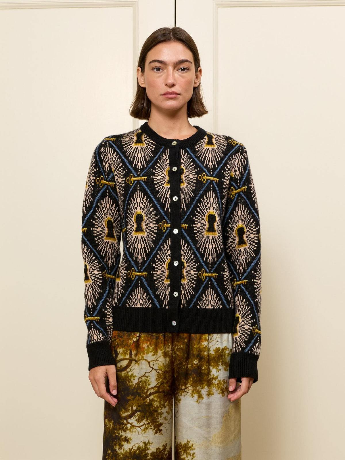 Front view of Getty Cardigan showcasing multicolor jacquard keyhole-and-diamond pattern, button-front, crew neck and ribbed cuffs on a cream paneled background