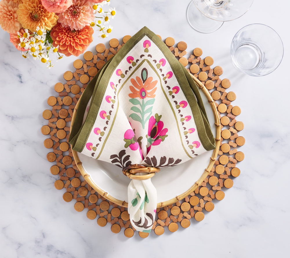 Top view of Pareo napkin in Multi folded in a napkin ring showing floral border and olive trim on a wooden bead placemat