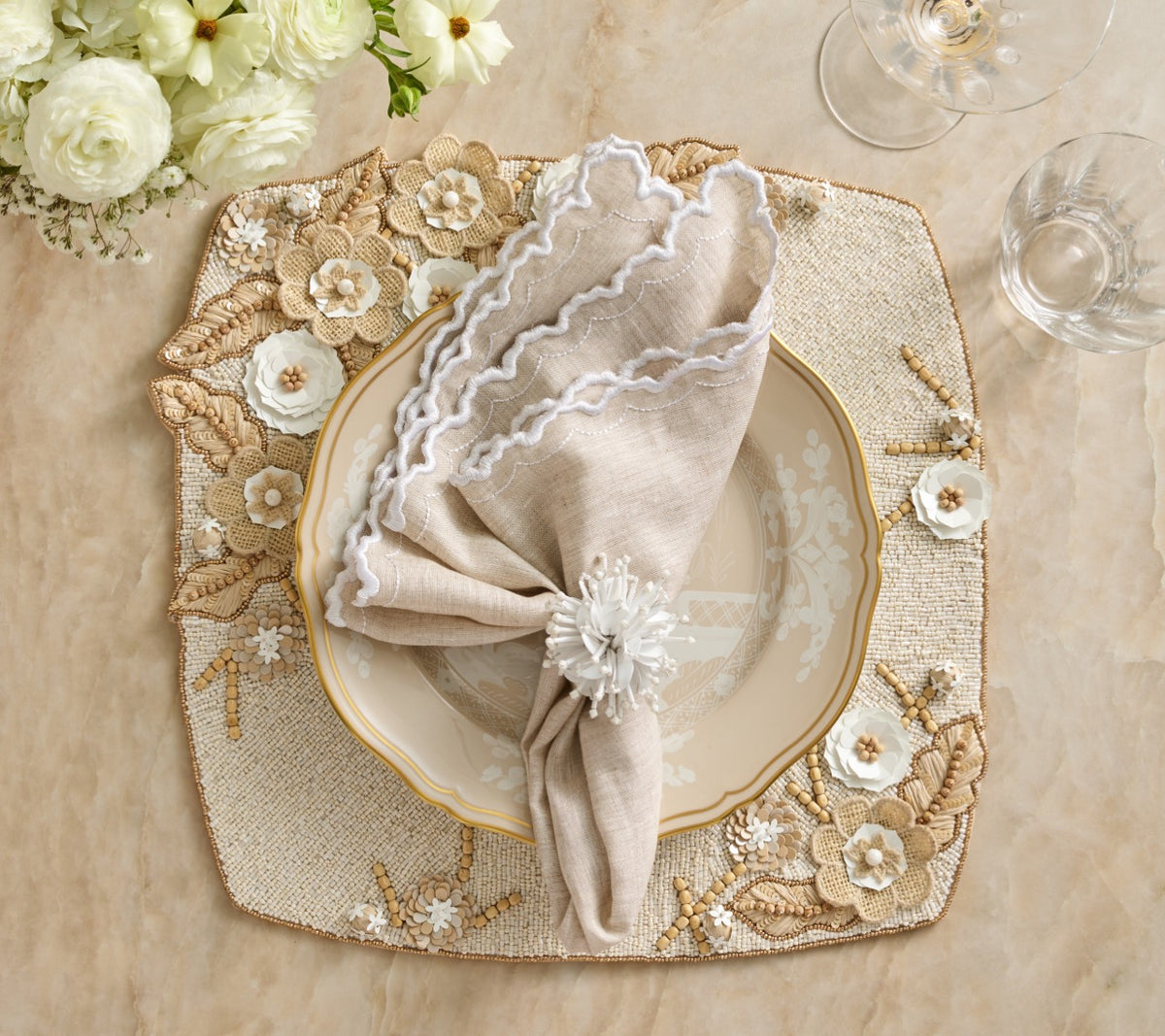 Top view of Arches linen napkin folded on plate with white scalloped embroidered edge and floral napkin ring