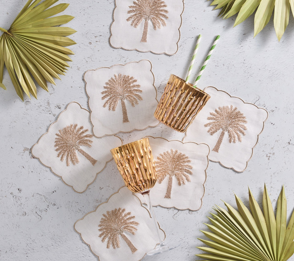 Top-down view of Date Palm linen cocktail napkins, set of 6, showing brown palm motifs, gold embroidery and scalloped edges