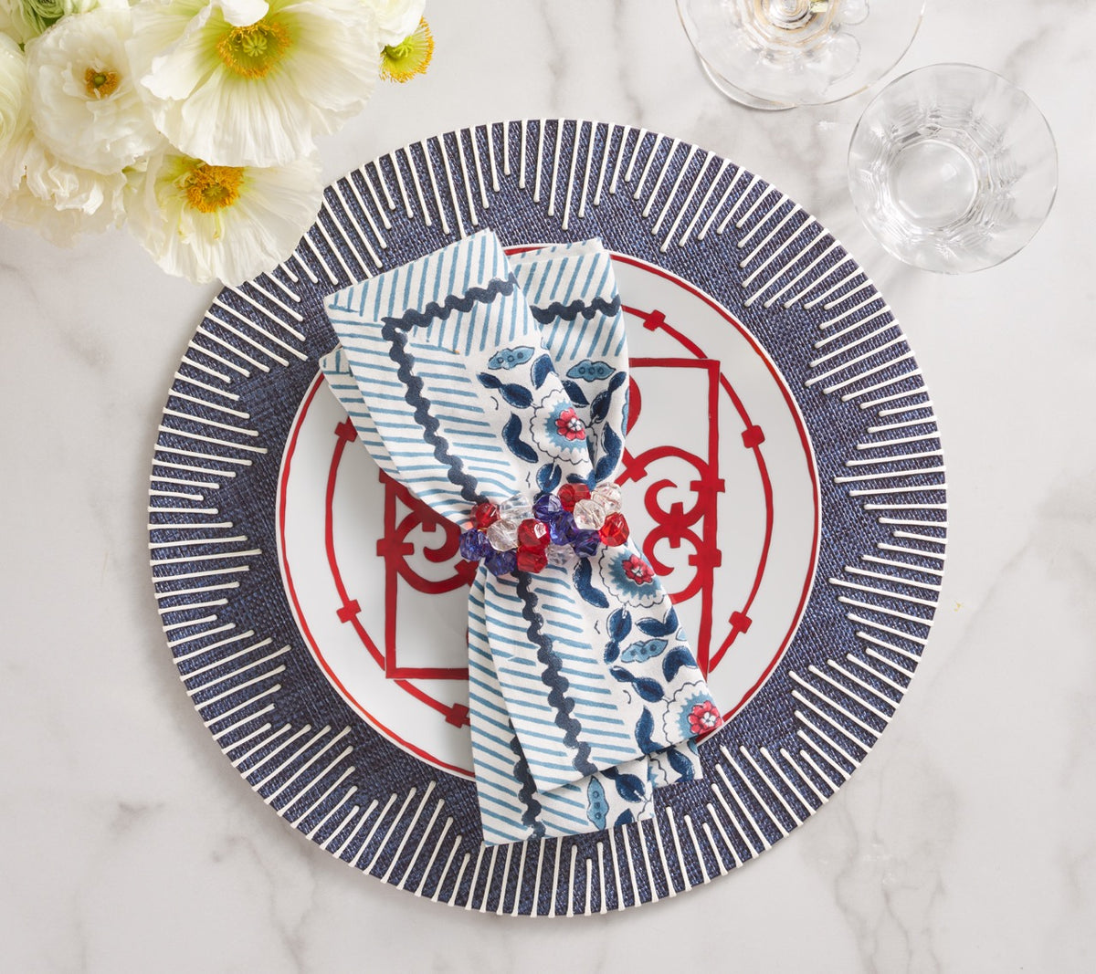 Top view of Pop Rocks napkin ring set showcasing red, white and blue bejeweled stones holding a folded patterned napkin on a red-and-blue charger plate