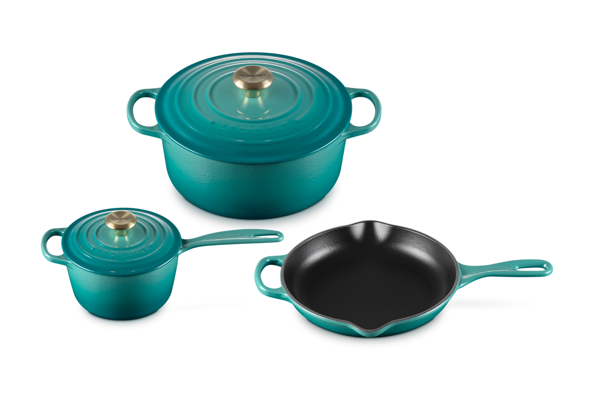 Three-quarter view of 5-piece Riviera enameled cookware set showing Dutch oven with lid, covered saucepan, and skillet on white background