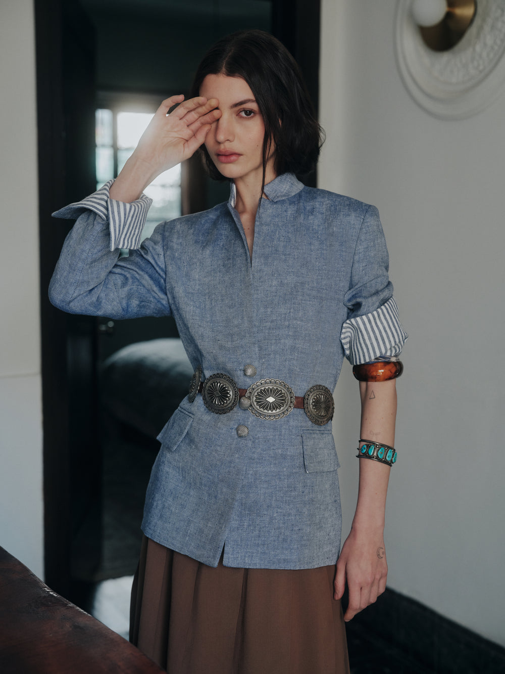 Front of Daisy Sailor blue linen blazer showing tailored fit, rolled striped cuffs, silver shell buttons, and concho belt in doorway